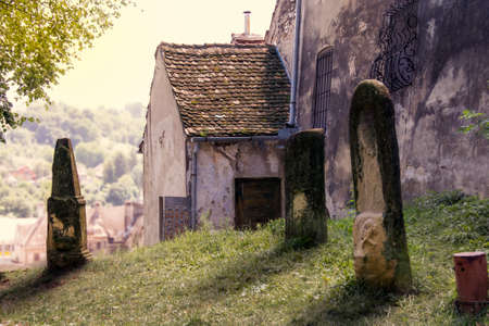 Colorful, warm scene in Romania (of some old and worn tombstones on a hill next to a historic House...