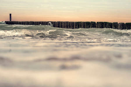 Waves with whitecaps break on the breakwater on a Dutch beach. The wave is approaching with high speed.の写真素材