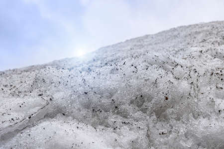 Close-up of melting snow on a hill with sunlight and a blue skyの写真素材