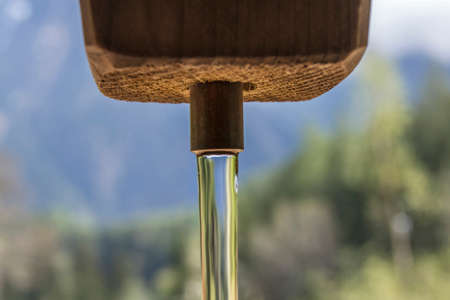 Pure and fresh mountain water streaming out of a primitive wooden tap somewhere in Austria.