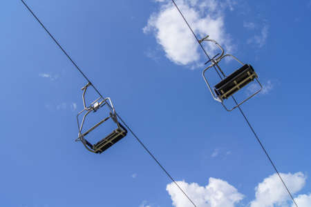 Two empty seats of a ski-lift against the background vivid blue sky with small white cloudsの写真素材