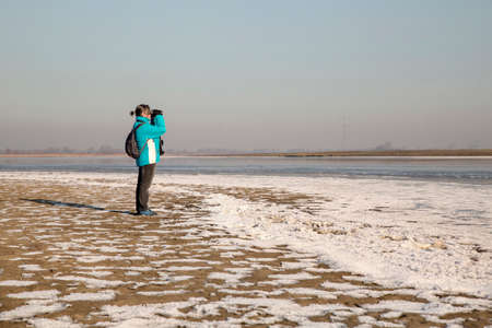 Woman looking through binoculars in a winter landscapeの写真素材