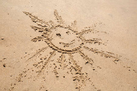 A drawing of a smiling sun in the wet sand on a beachの写真素材