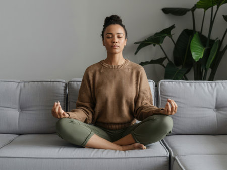 A serene scene of a woman meditating on a couch, with a plant in the background. The image captures the essence of mindfulness, relaxation, and inner peace.の素材