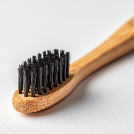 A natural bamboo toothbrush with dark bristles is shown from a close-up perspective on a white background.の素材
