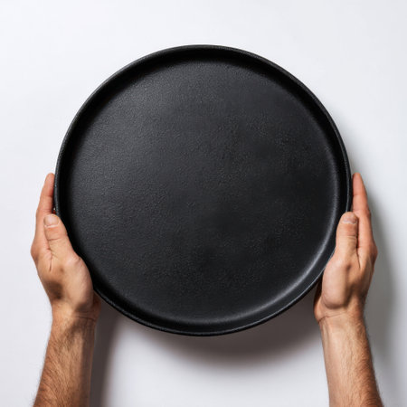 Two hands are holding a dark, textured, round serving tray against a white background, showcasing its surface.の素材