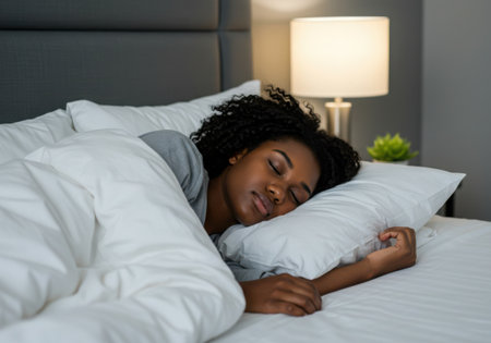 A woman is sleeping peacefully in her bed. She is covered with a white blanket and has her head on a pillow. The room is dark and quiet, perfect for a good night's rest.の素材