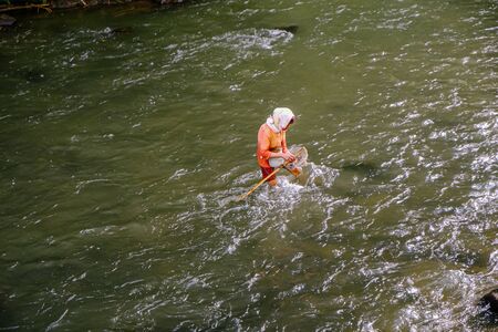 A woman catching freshwater fish in a river.