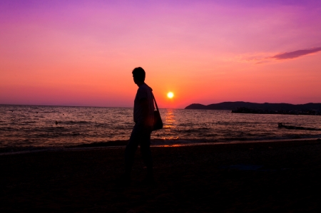 Man walking on the beach with sunset in backgroundの写真素材