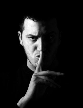 Man showing be quiet sign, low key and black and white techniques の写真素材