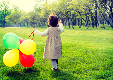 Little child holding the balloons and walking in parkの写真素材