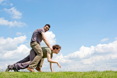 Men riding one over another with fluffy clouds in backgroundの写真素材