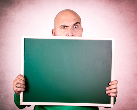 Suspicious bald man holding blank chalk boardの写真素材