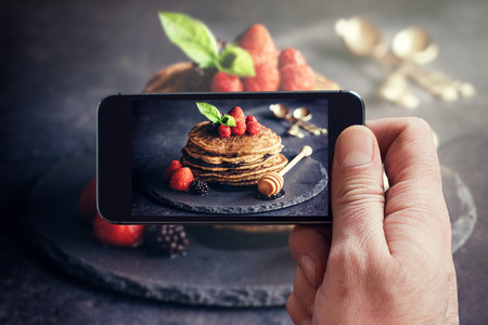 Man photographing wit his phone buckwheat pancakes with fruitの写真素材
