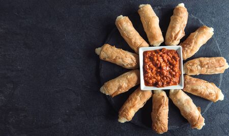 Homemade mini cheese pie sticks with ajvar salad on dark background with blnk space