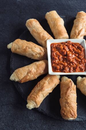 Homemade mini cheese pie sticks with ajvar salad on dark background