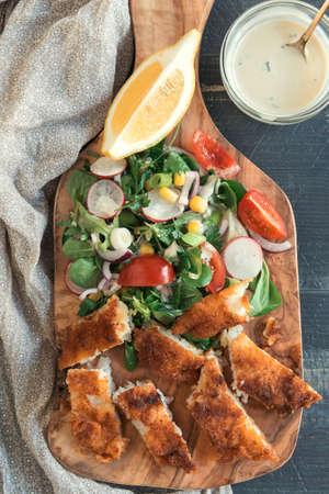 Served sliced catfish fillets with healthy salad on wooden boardの写真素材