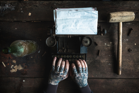 Writer with tattooed hand writing on old typing machine with blank paper,selective focusの写真素材