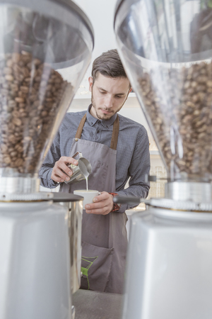 A barista pouring mil foam into cappuccinoの写真素材
