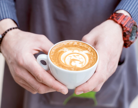 Barista holding cup of cappuccino with drawed English bulldog on the topの写真素材