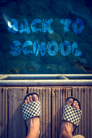 Man standing on the sea cliff with back to school sign in the waterの写真素材