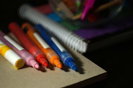 set of multi-colored acrylic markers with a notebook on a black background