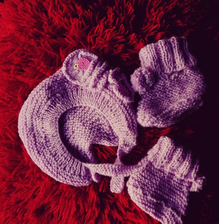 Knitted baby shoes, booties and hat on a red backgroundの写真素材