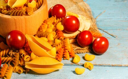 Organic food on a blue wooden background. A variety of types and forms of dry Italian pasta with vegetables, tomatoesの写真素材