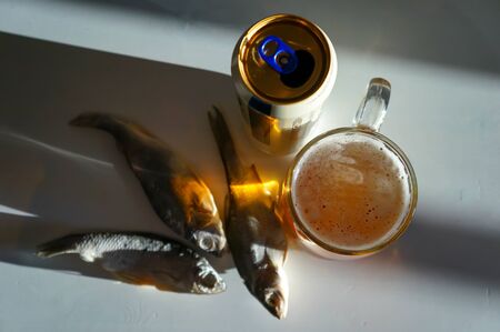 a glass of golden foamy fresh beer with salted fish for a snack