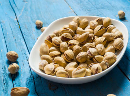 White bowl of pistachios on a wooden background, copy spaceの写真素材