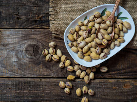 White bowl of pistachios on a wooden background, copy space