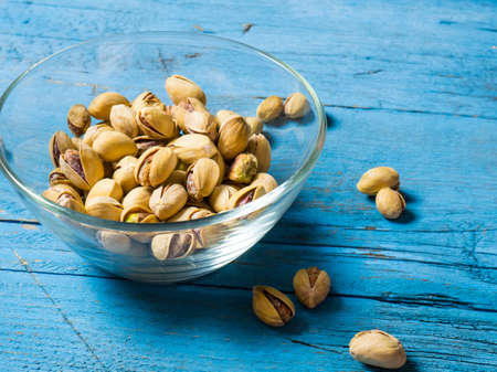 pistachios in a clear glass bowl on an old wooden table, an atmospheric rustic composition, a copy...