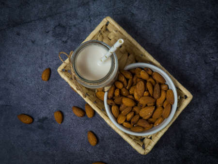 almond milk in a bottle and almonds in a wooden bowl, on a black stone background copyspace for textの写真素材