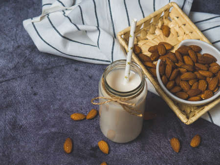 almond milk in a bottle and almonds in a wooden bowl, on a black stone background copyspace for textの写真素材