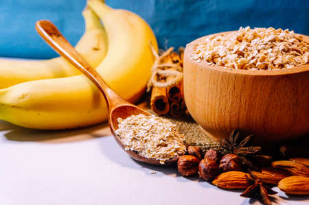 ingredients oatmeal in a wooden bowl and spoon with bananas, nuts and cinnamon, a healthy vegetarian breakfast with a place for inscriptionの写真素材