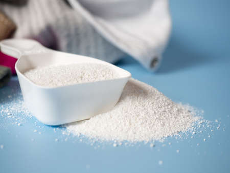 white dustpan with baby washing powder on the background of clothes. Detergent for washing...