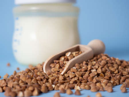 buckwheat porridge in a wooden spoon on the background of a baby bottle, milk porridge with prebiotics of baby formula. baby food concept, copy spaceの写真素材