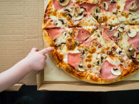 baby's hand reaches for pizza with ham and mushroomsの写真素材
