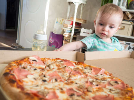 a small child reaches for a slice of pizzaの写真素材