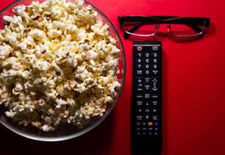 a glass bowl with popcorn and a TV remoteの写真素材