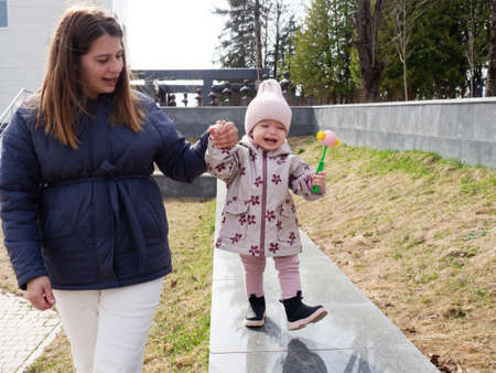 mom walks with a one-year-old baby by the hand in the parkの写真素材