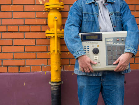 An old-school '90s drum machine in the hands of a beatmaker against a brick wall. Retro Digital...