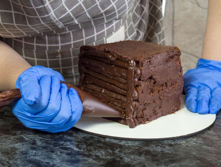 pastry chef girl makes chocolate cake smeared with ganache