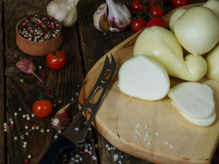 scamorza cheese.Italian caciocavallo cheese and red tomatoes on an old wooden table, rustic...