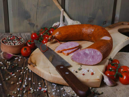 sliced sausage on a wooden board with garlic, tomatoes and pepper. Sausage and spices on an old...