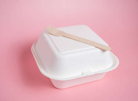 white paper food container and wooden fork on pink background, copy space