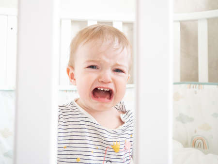 Portrait of a beautiful girl sitting in a crib and crying
