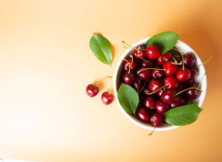 fresh cherries in a white bowl on an orange background with place for text