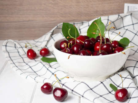 fresh cherries in a white bowl on a white wooden tableの写真素材
