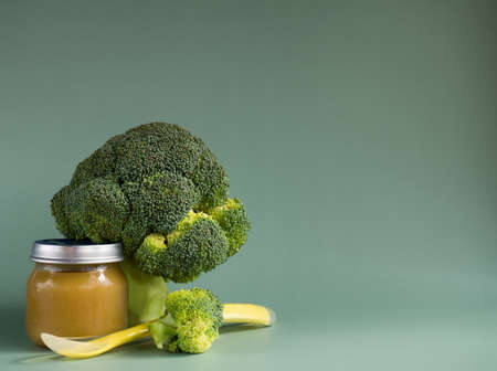 Glass jar with natural baby food on green background: vegetable puree with broccoli selective focusの写真素材
